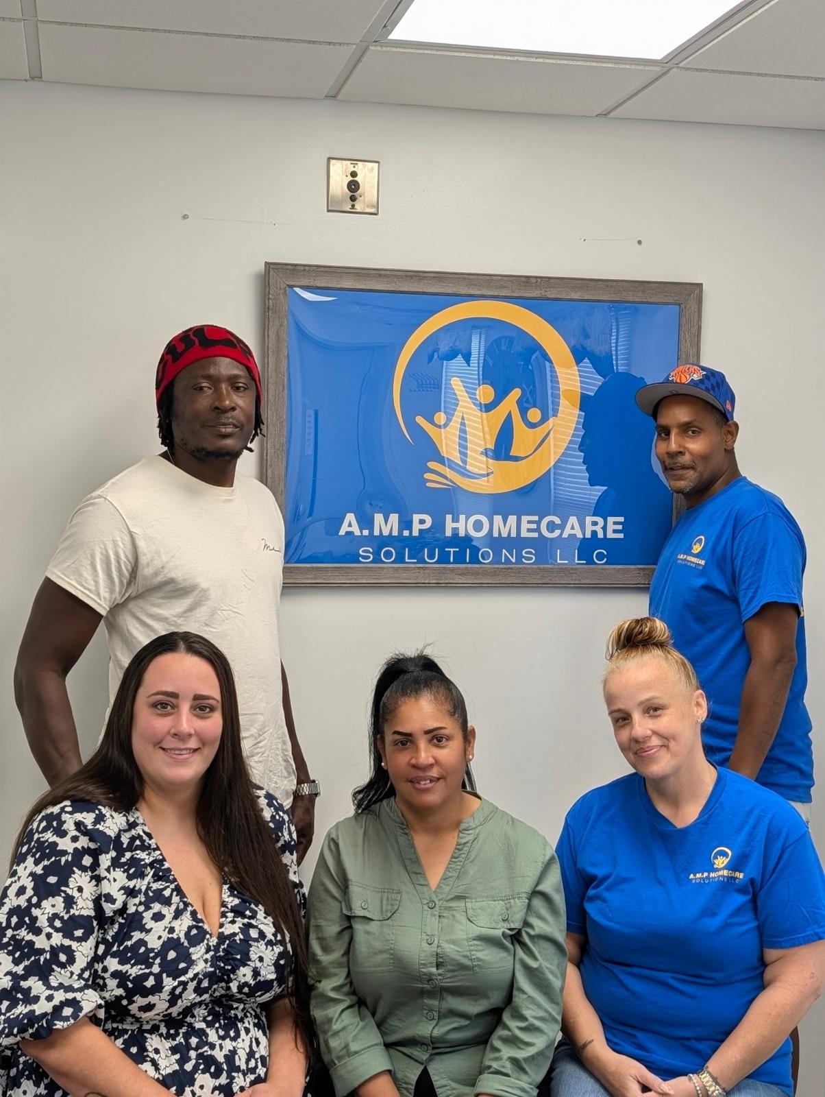 A.M.P HomeCare Solutions team of five posing in front of the branded company logo sign — celebrating 10 years